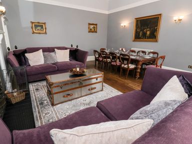 A living room with purple sofas a wooden dining table and framed paintings on gray walls at The Stables and West Wing Bolton Percy near Tadcaster