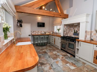 A kitchen with wooden countertops tiled floor stools under a counter and exposed wooden beams at The Stables and West Wing in Bolton Percy near Tadcaster