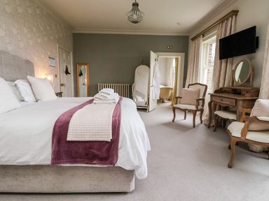 A bedroom with a large bed chairs a dressing table and a door leading to a bathroom at The Stables and West Wing Bolton Percy near Tadcaster