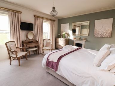 A bedroom with a bed and two chairs near windows with curtains at The Stables and West Wing in Bolton Percy near Tadcaster