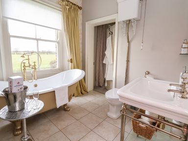 A bathroom with a clawfoot bathtub, a sink, a toilet, and a window with a view of fields at The Stables and West Wing Bolton Percy near Tadcaster