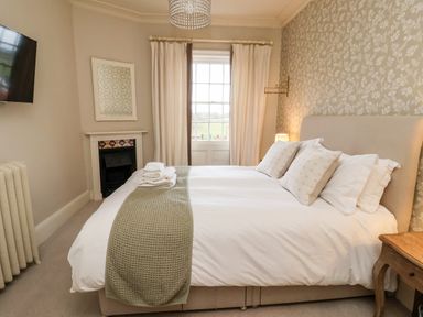 A bedroom with a bed near a window with curtains and a wall-mounted television at The Stables and West Wing in Bolton Percy near Tadcaster