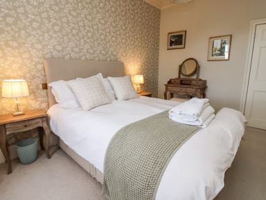A bedroom with a bed white bedding pillows bedside tables lamps a wooden dressing table and framed pictures on the wall at The Stables and West Wing Bolton Percy near Tadcaster