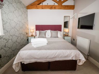A bedroom with a double bed bedside tables lamps and a wall-mounted TV at The Stables and West Wing in Bolton Percy near Tadcaster