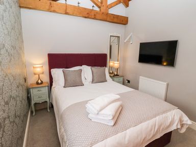 A bedroom with a double bed towels on the bed nightstands with lamps wall mirror and a wall mounted television at The Stables and West Wing Bolton Percy near Tadcaster
