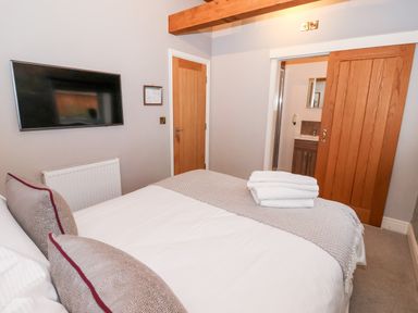 A bedroom with a bed a television on the wall and a wooden door leading to a bathroom at The Stables and West Wing Bolton Percy near Tadcaster