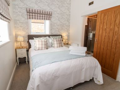 A bedroom with a bed pillows bedside tables lamps a window with blinds and a wooden sliding door at The Stables and West Wing in Bolton Percy near Tadcaster