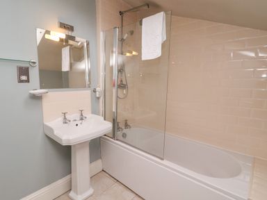A bathroom with a pedestal sink and a bathtub with a glass shower screen at The Stables and West Wing Bolton Percy near Tadcaster