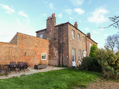 An outdoor area with brick walls a patio table with chairs and a two story brick building with windows and chimneys at The Stables and West Wing in Bolton Percy near Tadcaster