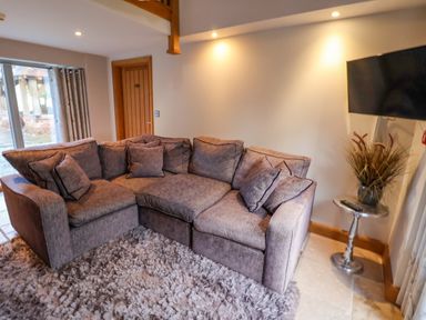 A living room with a sectional sofa a shaggy rug a side table with a plant and a wall-mounted TV at Servant's Quarters in Bolton Percy near Tadcaster