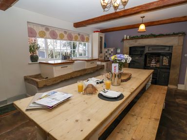 A kitchen with a wooden dining table set with glasses of orange juice a teapot and flowers near a window and an old fireplace at Servant's Quarters Bolton Percy near Tadcaster