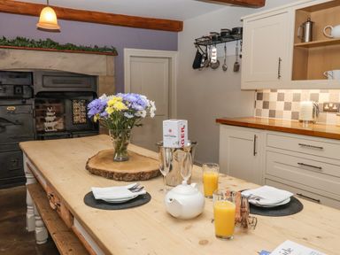 A kitchen with a wooden table set with two glasses of orange juice a teapot plates and cutlery a vintage stove and cream cabinets at Servant's Quarters Bolton Percy near Tadcaster