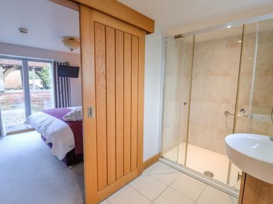 A bedroom with a bed and television partially visible through a wooden sliding door next to a bathroom with a shower and sink at Servant's Quarters Bolton Percy near Tadcaster
