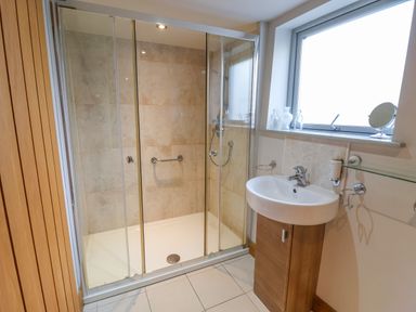 A bathroom with a glass-enclosed shower and a sink with a wooden cabinet beneath a window at Servant's Quarters in Bolton Percy near Tadcaster