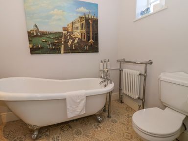 A bathroom with a clawfoot bathtub a toilet a radiator and a painting of a canal scene on the wall at Servant's Quarters Bolton Percy near Tadcaster