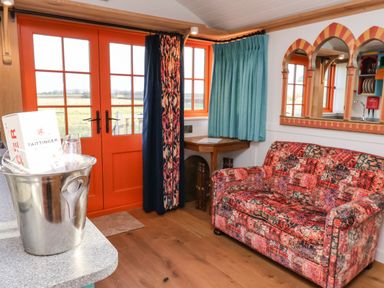 A room with orange framed glass doors curtains a patterned sofa a wooden corner table and a silver ice bucket with bottles at The Storyteller in Bolton Percy near Tadcaster