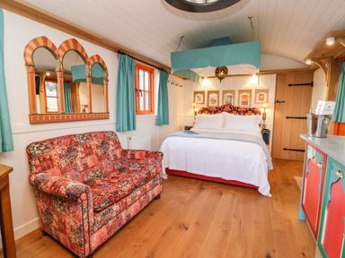 A bedroom with a bed, a patterned sofa, colorful curtains, a mirror on the wall, and a decorated cabinet at The Storyteller in Bolton Percy near Tadcaster