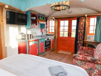 A small living space with colorful kitchen cabinets a mounted television a patterned sofa and orange double doors at The Storyteller in Bolton Percy near Tadcaster