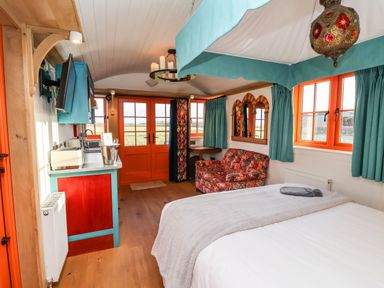 A bedroom with a bed a sofa a kitchen area and orange window frames at The Storyteller in Bolton Percy near Tadcaster