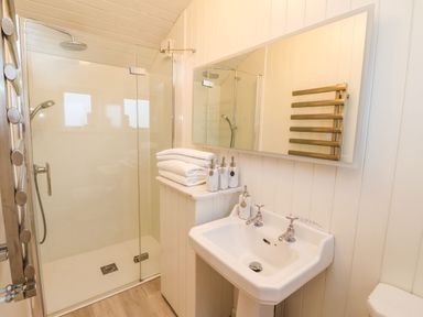 A bathroom with a glass shower enclosure a sink with two taps towels and soap dispensers at The Storyteller in Bolton Percy near Tadcaster