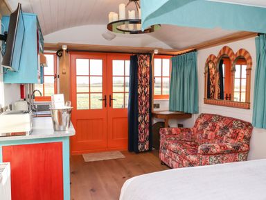 A room with orange doors, a patterned sofa, turquoise curtains, a kitchen counter, and a wall mirror at The Storyteller in Bolton Percy near Tadcaster