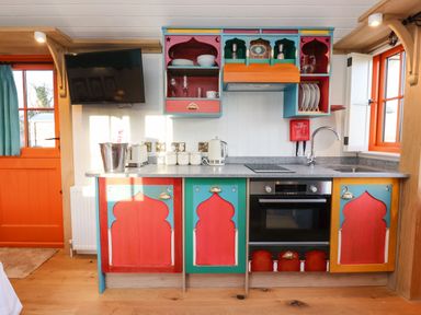 A kitchen with colorful cabinets a black oven a television on the wall and a sink with a faucet at The Storyteller in Bolton Percy near Tadcaster