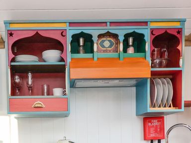 A kitchen cabinet with plates bowls glasses and a fire blanket at The Storyteller in Bolton Percy near Tadcaster