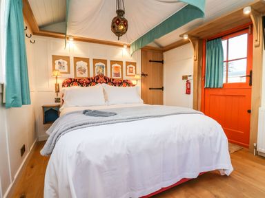 A bedroom with a bed a red patterned headboard blue curtains and an orange door at The Storyteller in Bolton Percy near Tadcaster