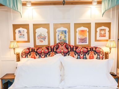 A bedroom with a patterned headboard wall art two lamps and white pillows at The Storyteller in Bolton Percy near Tadcaster