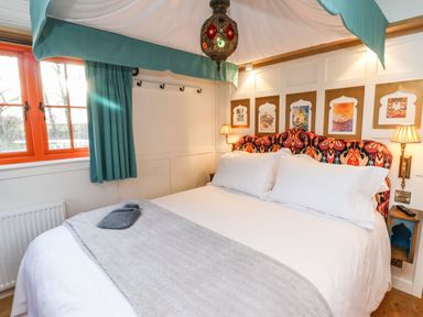 A bedroom with a large bed with white bedding and a gray blanket near a window with teal curtains at The Storyteller in Bolton Percy near Tadcaster
