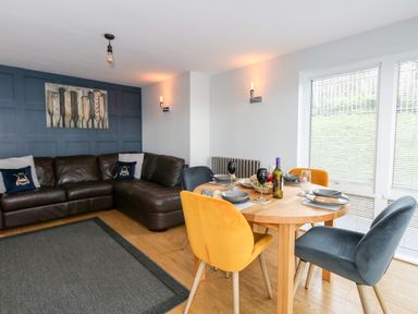 A living room with a brown leather corner sofa and a wooden dining table with colorful chairs at Pointers View in Weymouth