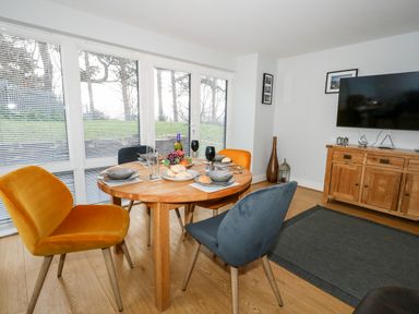 A dining area with a round wooden table set with four plates and glasses and four chairs in front of large windows at Pointers View in Weymouth