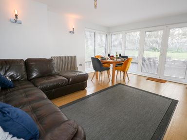 A living room with a brown leather sofa a dining table with four chairs and large windows with blinds at Pointers View in Weymouth