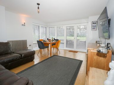 A living room with brown leather sofas a round dining table with chairs and a wall-mounted television at Pointers View in Weymouth