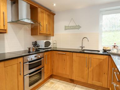 A kitchen with wooden cabinets black countertops a stainless steel oven a microwave and a sink at Pointers View in Weymouth
