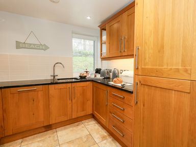 A kitchen with wooden cabinets a black countertop a window and appliances at Pointers View in Weymouth