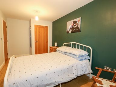 A bedroom with a white metal bed frame and bedding next to a wooden nightstand under a green wall with a painting and wooden doors at Pointers View in Weymouth