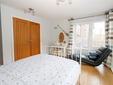 A bedroom with a white bed frame a wooden wardrobe a vanity table with a mirror and a black chaise lounge at Pointers View in Weymouth
