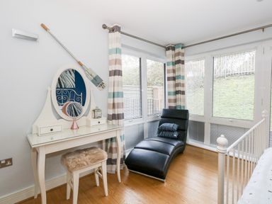 A corner of a room with a white dressing table and mirror a black chaise lounge and striped curtains at Pointers View in Weymouth