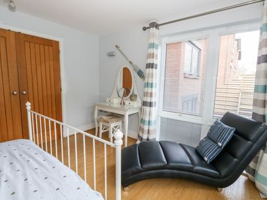 A bedroom with a white metal bed frame a wooden floor a black chaise lounge chair blue striped pillows a white vanity table with mirror and stool and wooden double closet doors at Pointers View in Weymouth