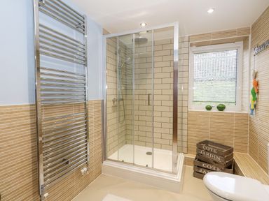 A bathroom with a glass shower enclosure a window with blinds a heated towel rail and wooden crates at Pointers View in Weymouth