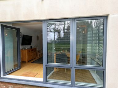 A view through windows showing a dining area with chairs and a living room with a wooden cabinet and a wall-mounted television at Pointers View in Weymouth