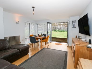 A living room with a dining table and chairs, a leather sofa, a wall-mounted TV, wooden sideboard, and an open door leading to a garden at Pointers View in Weymouth