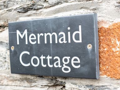 A sign with the words Mermaid Cottage on a stone wall at Mermaid Cottage in Port Isaac
