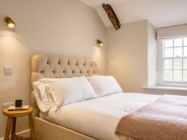 A bedroom with a bed a wooden side table a window and wall lights at Mermaid Cottage in Port Isaac