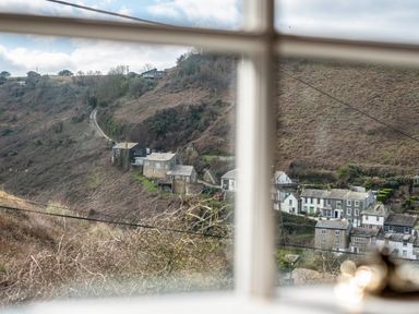 A view of houses on a hillside seen through a window at Mermaid Cottage in Port Isaac