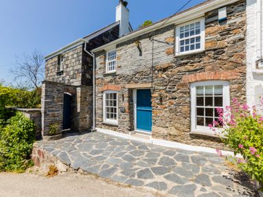 Stone cottage with blue door and windows and stone patio with flowers at Mermaid Cottage in Port Isaac