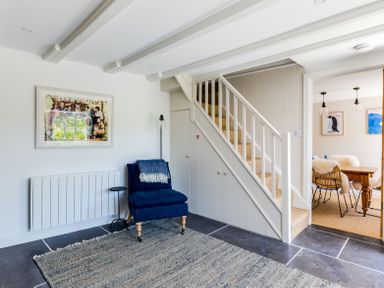 A sitting area with a blue chair and a small side table next to stairs and a dining room in Mermaid Cottage in Port Isaac