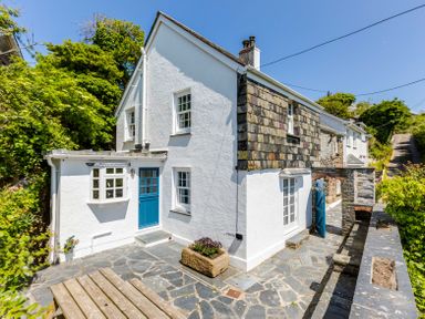 White cottage with blue doors and slate patio surrounded by greenery at Mermaid Cottage in Port Isaac