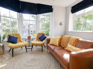 A sitting area with two yellow chairs and a brown sofa with cushions near large windows at Flat 6 Thornlow Heights Weymouth